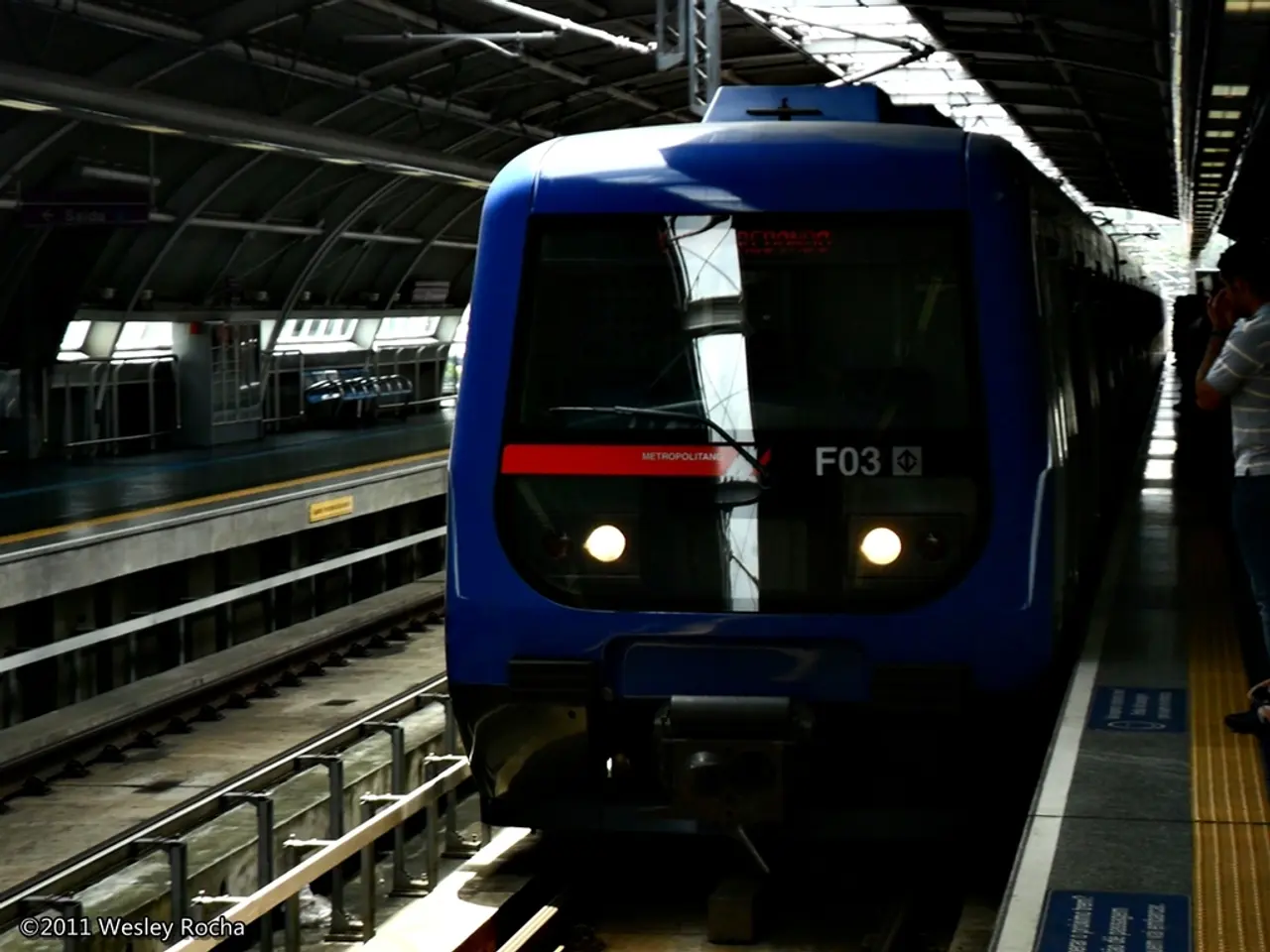 Here we can see a train on a railway track and on the right there are few persons standing on a...