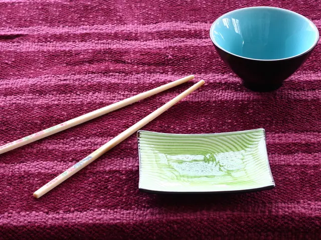 This picture describe about a blue bowl placed on the cloth and two Chinese sticks, beside we can...