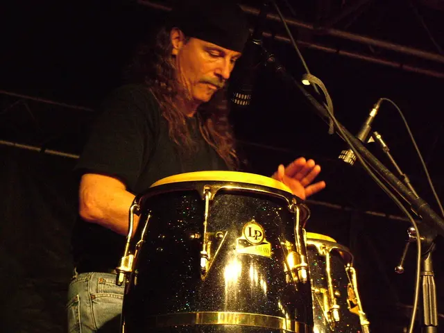 In the middle of the image a man is standing and playing drum. Bottom right side of the image there...