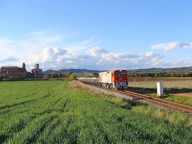 In the picture I can see a train is moving on the railway track, here I can see grass, current...