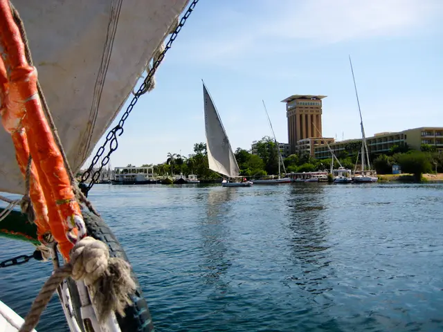 In the foreground of this picture, there are rods, rope, mainsail, boom of a boat. In the...