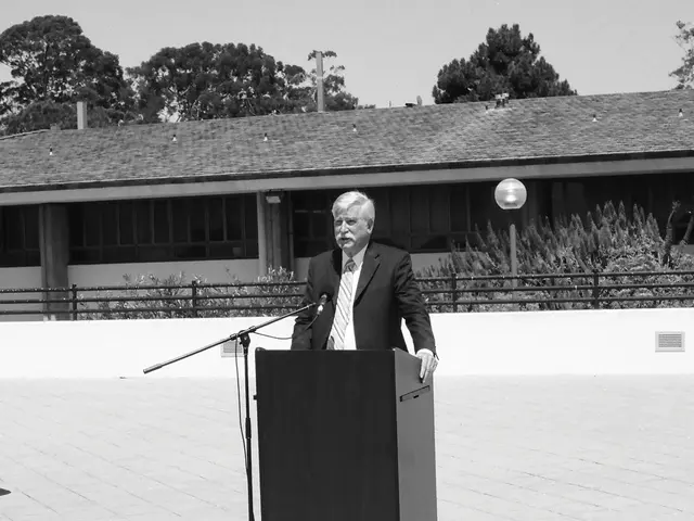 It is the black and white image in which there is a man standing in front of the podium. There is a...